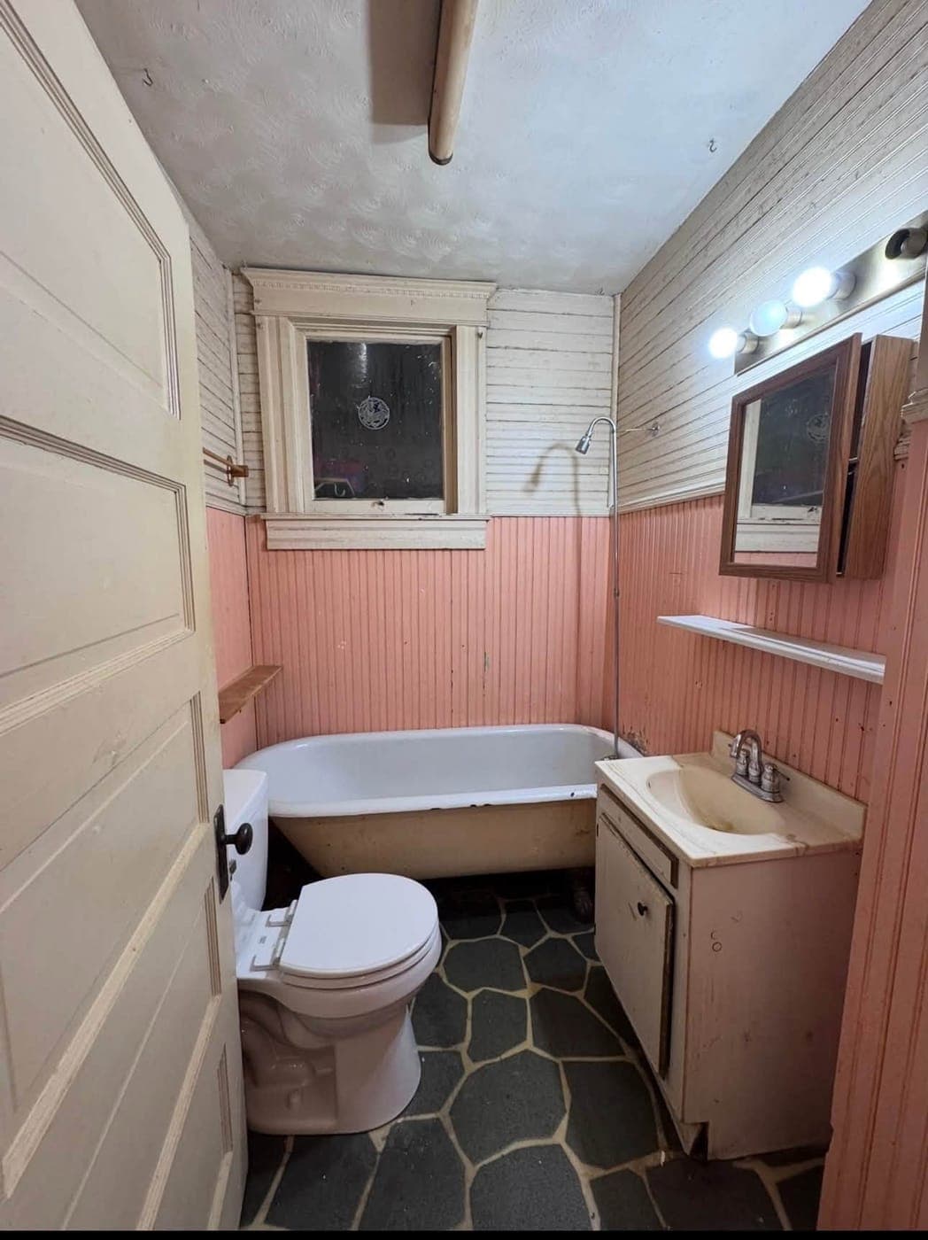 Vintage bathroom before remodel — aged clawfoot tub and paneling
